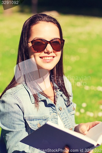 Image of smiling young girl with book sitting in park