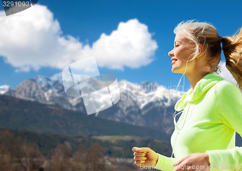 Image of happy young woman with earphones jogging outdoors