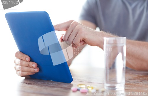 Image of close up of hands with tablet pc, pills and water