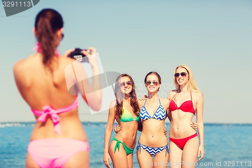 Image of group of smiling women photographing on beach