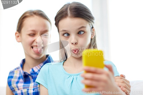 Image of happy girls with smartphone taking selfie at home