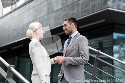 Image of smiling businessmen shaking hands on street