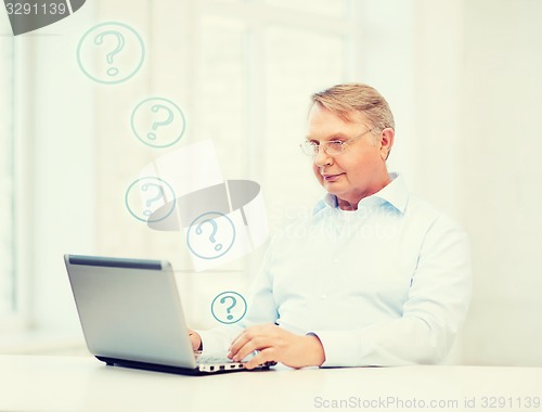 Image of old man in eyeglasses working with laptop at home