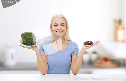 Image of smiling woman with broccoli and donut on kitchen