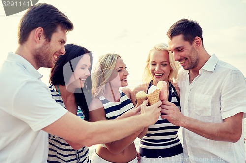 Image of smiling friends eating ice cream on beach