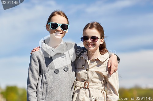 Image of happy little girls in sunglasses hugging outdoors