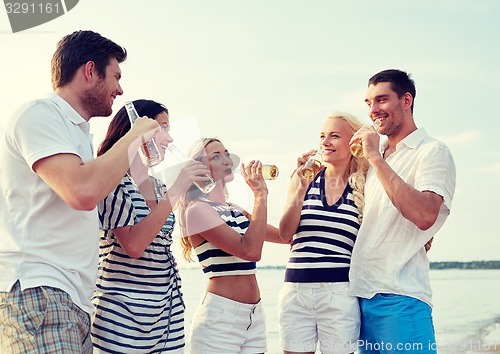 Image of smiling friends with drinks in bottles on beach