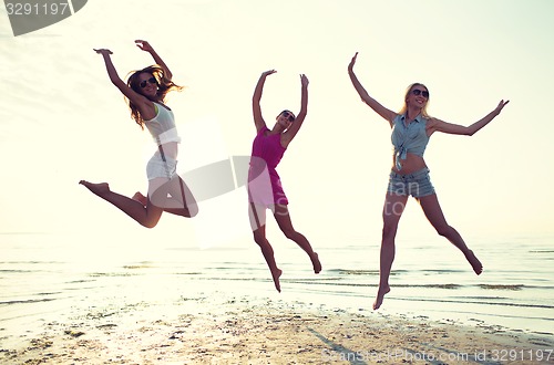 Image of happy female friends dancing and jumping on beach