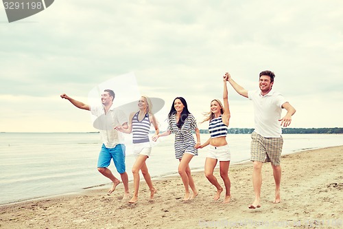 Image of smiling friends in sunglasses running on beach
