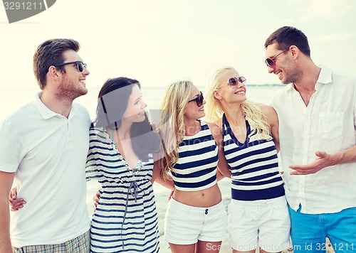 Image of smiling friends in sunglasses talking on beach