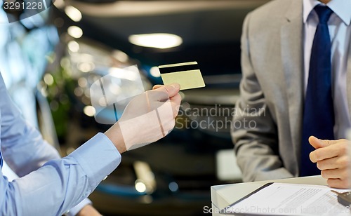 Image of customer giving credit card to car dealer in salon
