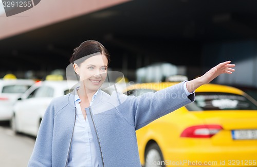 Image of smiling young woman waving hand and catching taxi