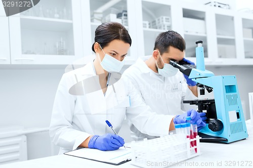 Image of scientists with clipboard and microscope in lab