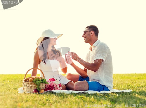 Image of smiling couple with small red gift box on picnic