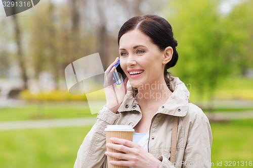 Image of smiling woman with smartphone and coffee in park