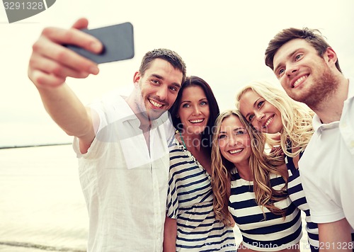 Image of happy friends on beach and taking selfie