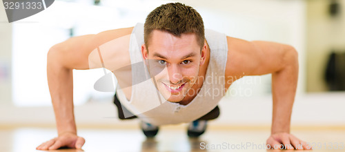 Image of smiling man doing push-ups in the gym