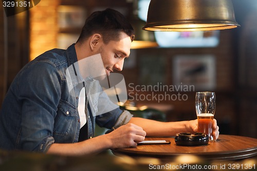 Image of man with smartphone and beer texting at bar