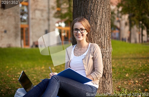 Image of happy student girl writing to notebook at campus