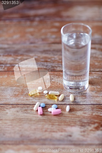 Image of pills and capsules with glass of water on table