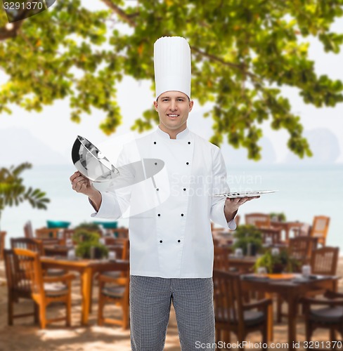 Image of happy male chef cook opening cloche