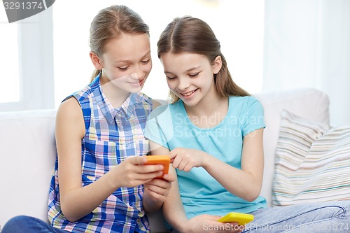 Image of happy girls with smartphones sitting on sofa