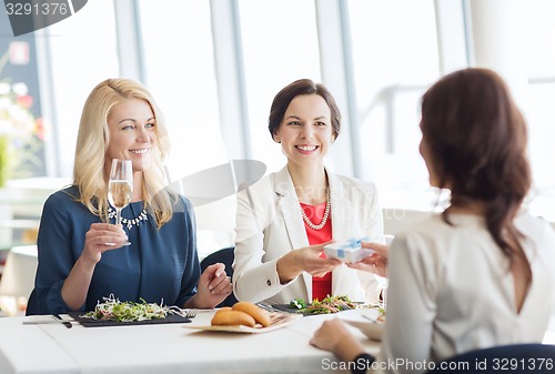 Image of happy women giving birthday present at restaurant