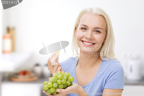 Image of happy woman eating grapes on kitchen