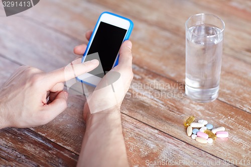 Image of close up of hands with smartphone, pills and water