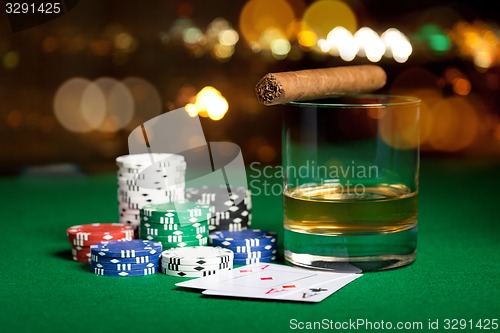 Image of close up of chips, cards whisky and cigar on table