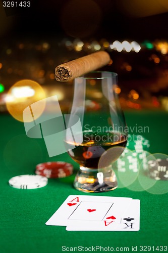 Image of close up of chips, cards whisky and cigar on table