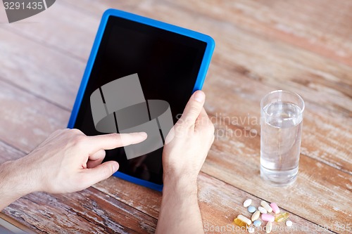 Image of close up of hands with tablet pc, pills and water