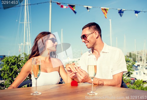 Image of smiling couple with champagne and gift at cafe