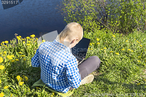 Image of Ten year boy with laptop on riverside in summer