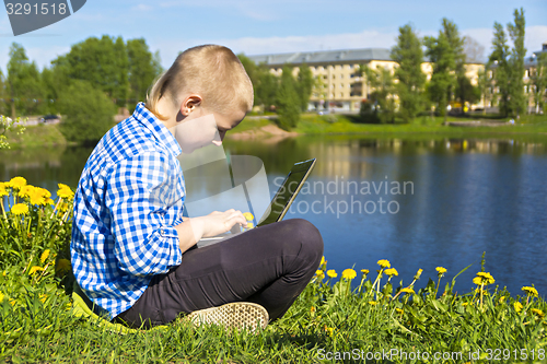 Image of Ten year boy with laptop on riverside