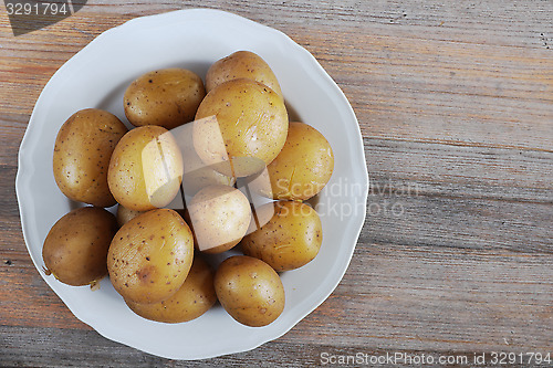 Image of boiled potatoes in their skins on a plate, wooden background