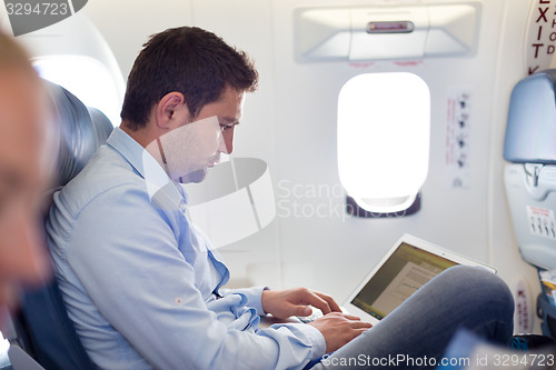 Image of Businessman working with laptop on airplane.