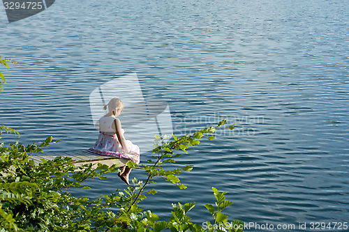 Image of Girl in summer dress sitting at deck over water