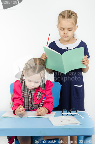 Image of Teacher standing behind the pupil looks notebook