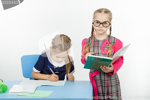 Image of The student writes in a notebook under supervision of teacher