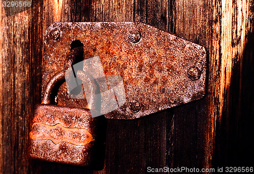 Image of Old rusty padlock on very old weather beaten door in brownish colours.