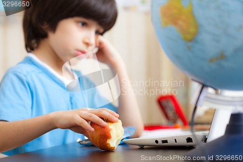 Image of boy sitting with a laptop and eating apple