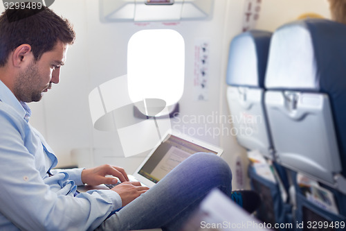 Image of Businessman working with laptop on airplane.