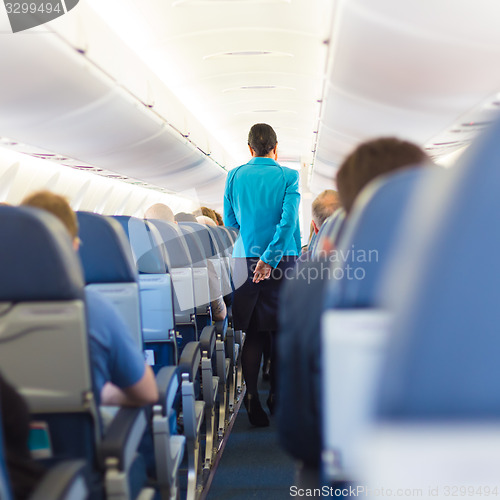 Image of Interior of airplane with stewardess walking the aisle.