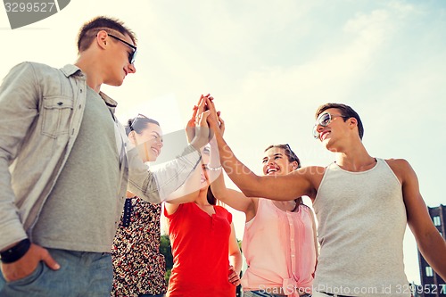 Image of group of smiling friends making high five outdoors