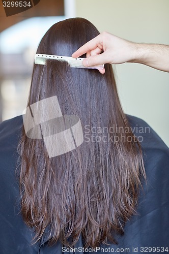 Image of hand with comb combing woman hair at salon