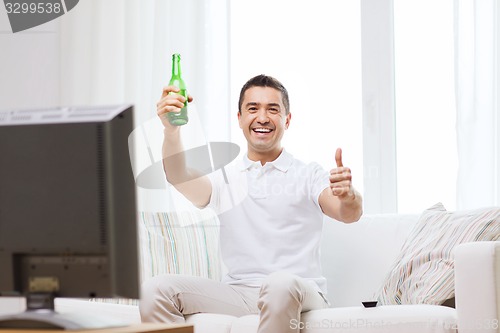 Image of smiling man watching tv and drinking beer at home