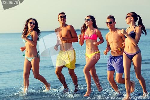 Image of smiling friends in sunglasses running on beach