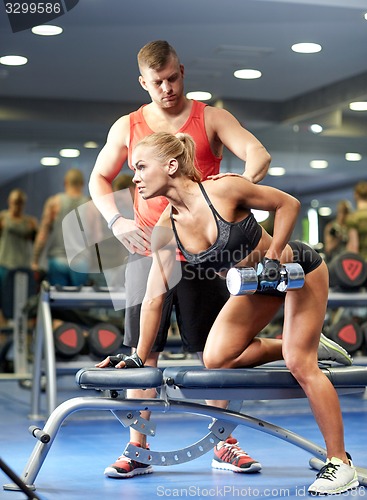 Image of young couple with dumbbell flexing muscles in gym