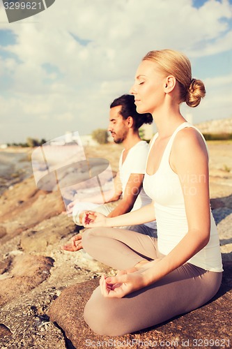 Image of smiling couple making yoga exercises outdoors